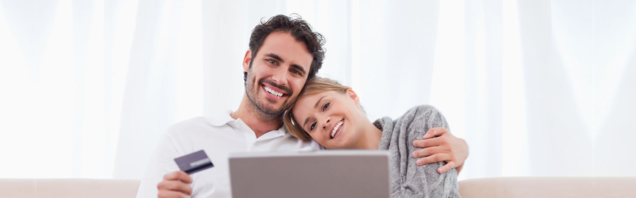 Couple smiling at their computer with their credit card in his hand