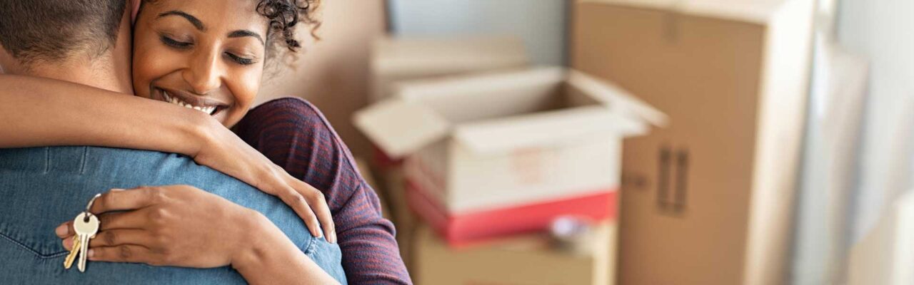 couple hugging about closing on their new home, with moving boxes in the background